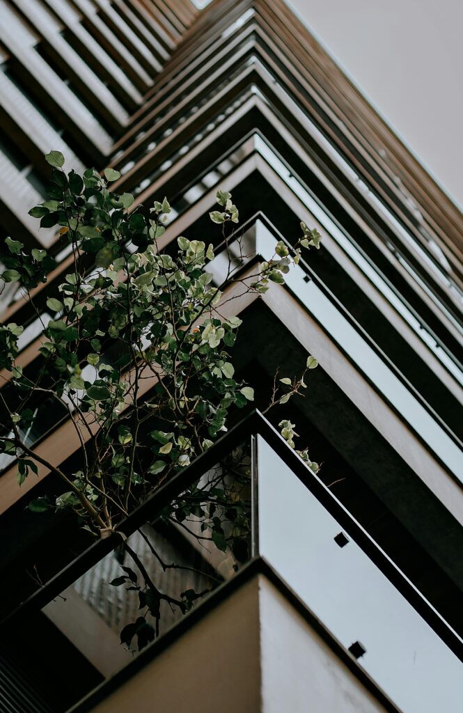 Low angle shot of a modern skyscraper with green plants providing urban greenery contrast.