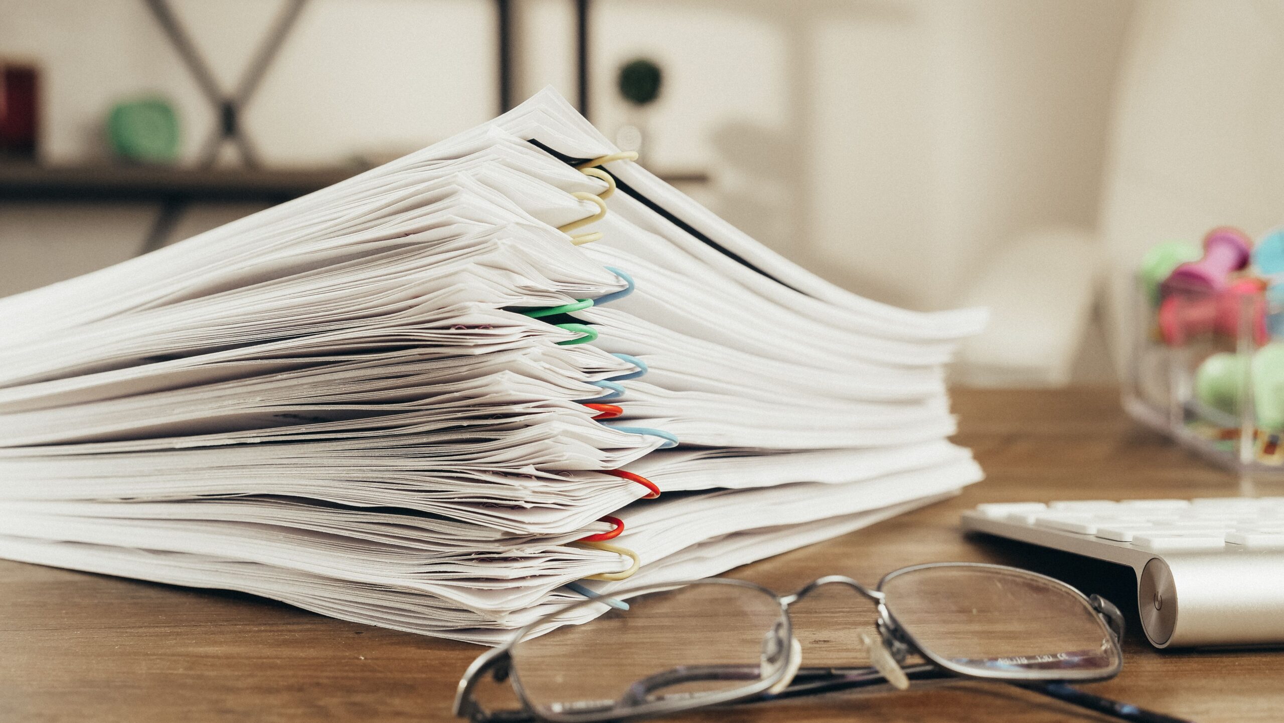 Close-up of a stack of office papers on a desk with glasses, emphasizing organization.